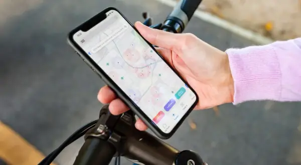 Dłoń trzyma smartfon z mapą i ikonami aplikacji rowerowych, oparty o kierownicę roweru.