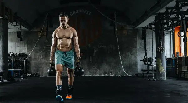 Mężczyzna z imponującą muskulaturą idzie z odważnikami w siłowni. To dowód, że crossfit dla kogo? Dla każdego, kto chce budować siłę i wytrzymałość!