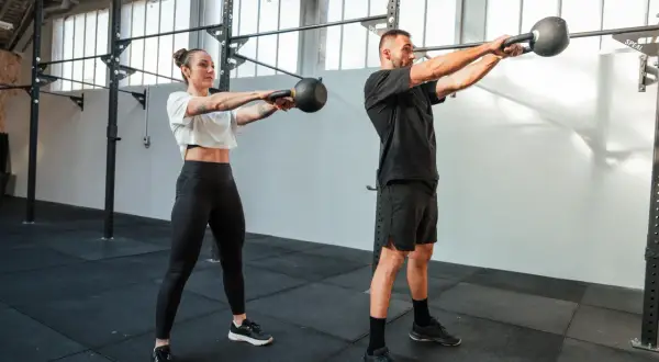 Kobieta i mężczyzna ćwiczą z kettlebellami w siłowni.