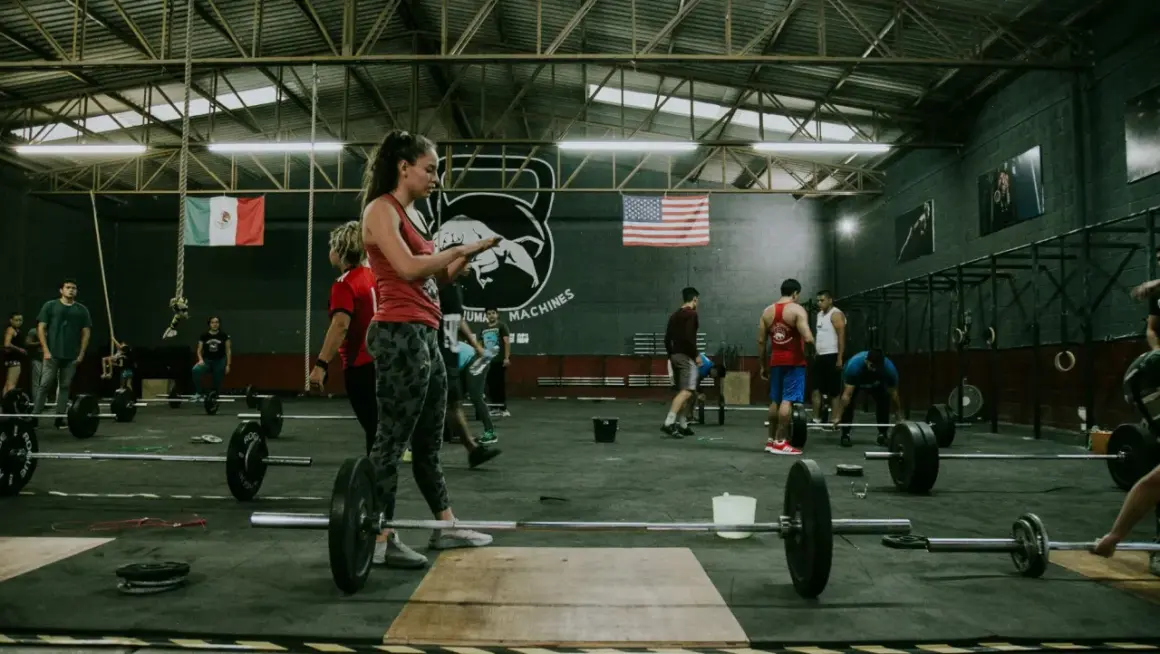 Ludzie ćwiczą w siłowni crossfit. Zastanawiasz się, crossfit po jakim czasie efekty? Widoczni są zawodnicy i sprzęt do treningu.