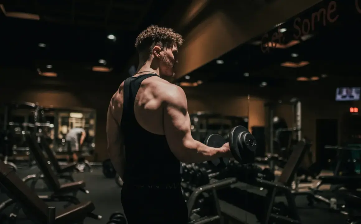 Mężczyzna ćwiczy biceps z hantlem w siłowni. To dowód, jak crossfit zmienił moje życie, budując siłę i pewność siebie.