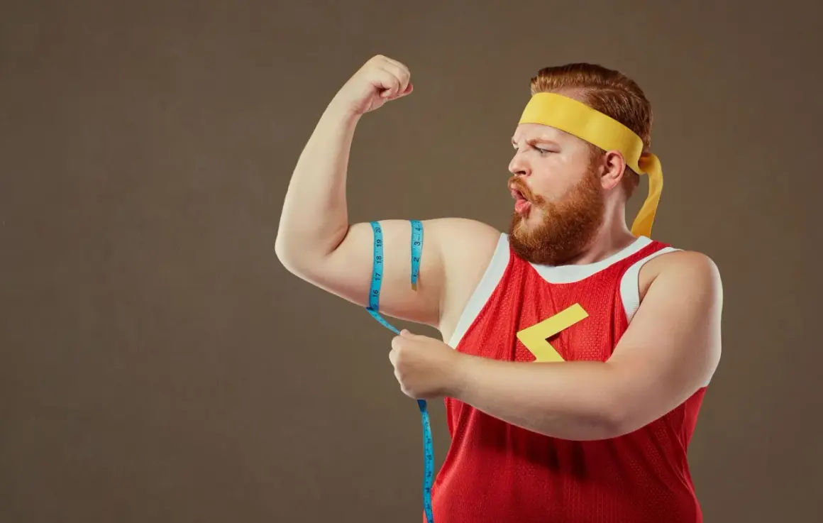 Mężczyzna typu endomorfik z wąsami i brodą, w żółtej opasce i czerwonej koszulce, mierzy obwód bicepsa.