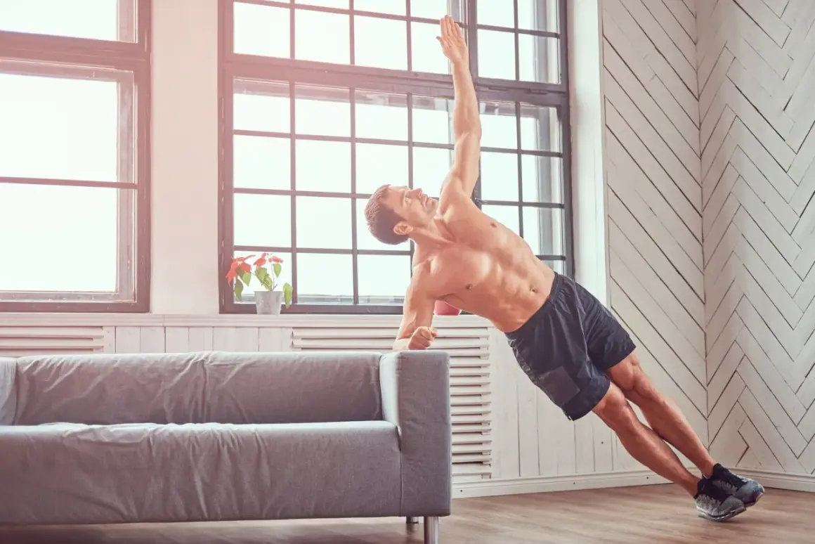 Mężczyzna ćwiczy crossfit w domu, wykonując deskę boczną na kanapie. Pokazuje, jak ćwiczyć crossfit w domu bez sprzętu.