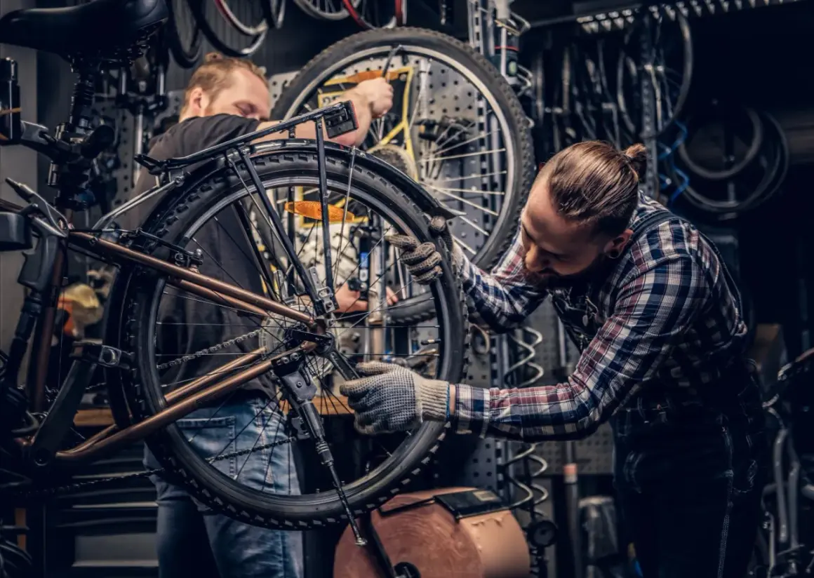 Dwóch mechaników pracuje nad rowerem w warsztacie. Jeden z nich dokonuje konserwacji roweru, dokręcając śruby kluczem.