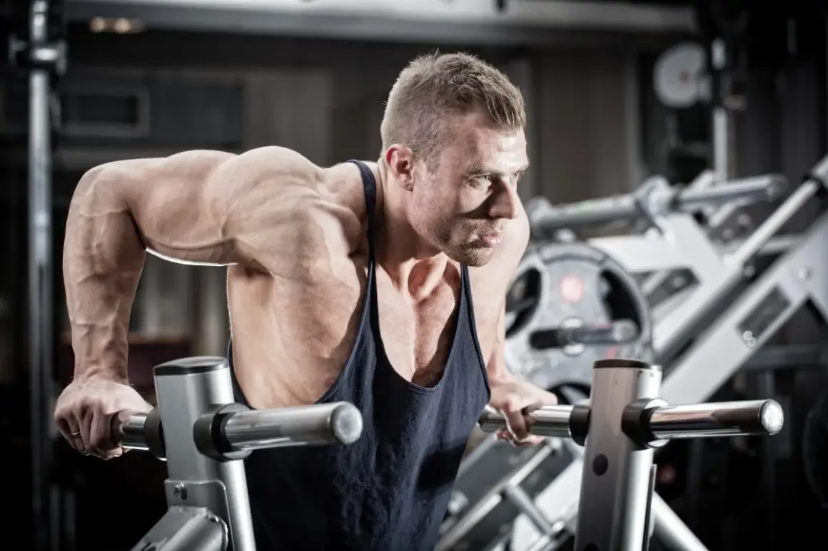 Mięśniowy mężczyzna wykonuje pompki na poręczach, jedno z najlepszych ćwiczeń na triceps.