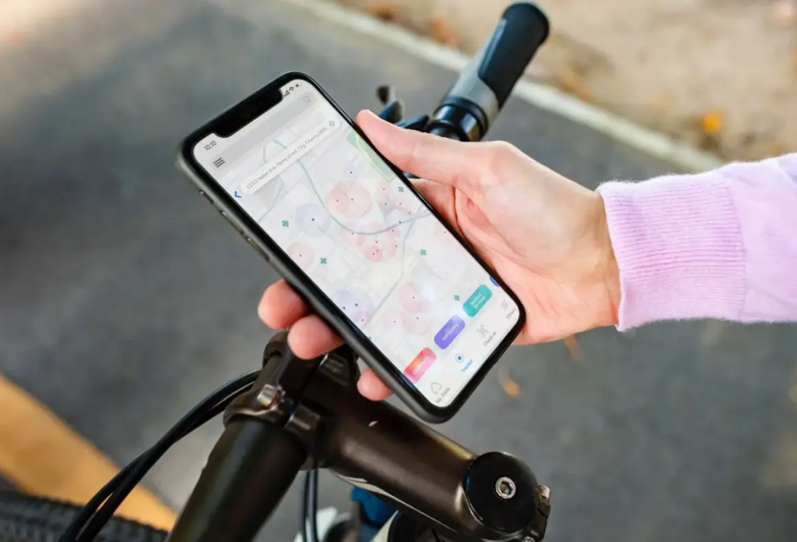 Dłoń trzyma smartfon z mapą i ikonami aplikacji rowerowych, oparty o kierownicę roweru.