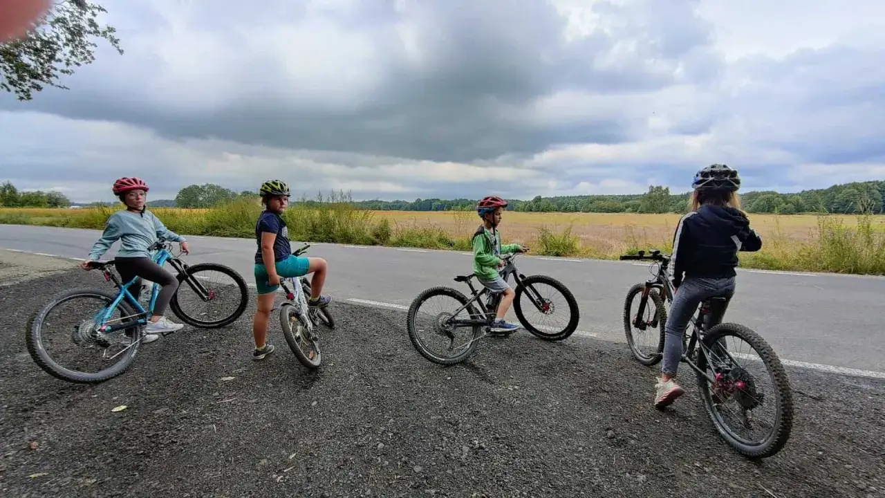 Cztery dzieci na rowerach, każdy z nich ma rower 20 cali na jaki wzrost. Dzieci w kaskach stoją na poboczu drogi.