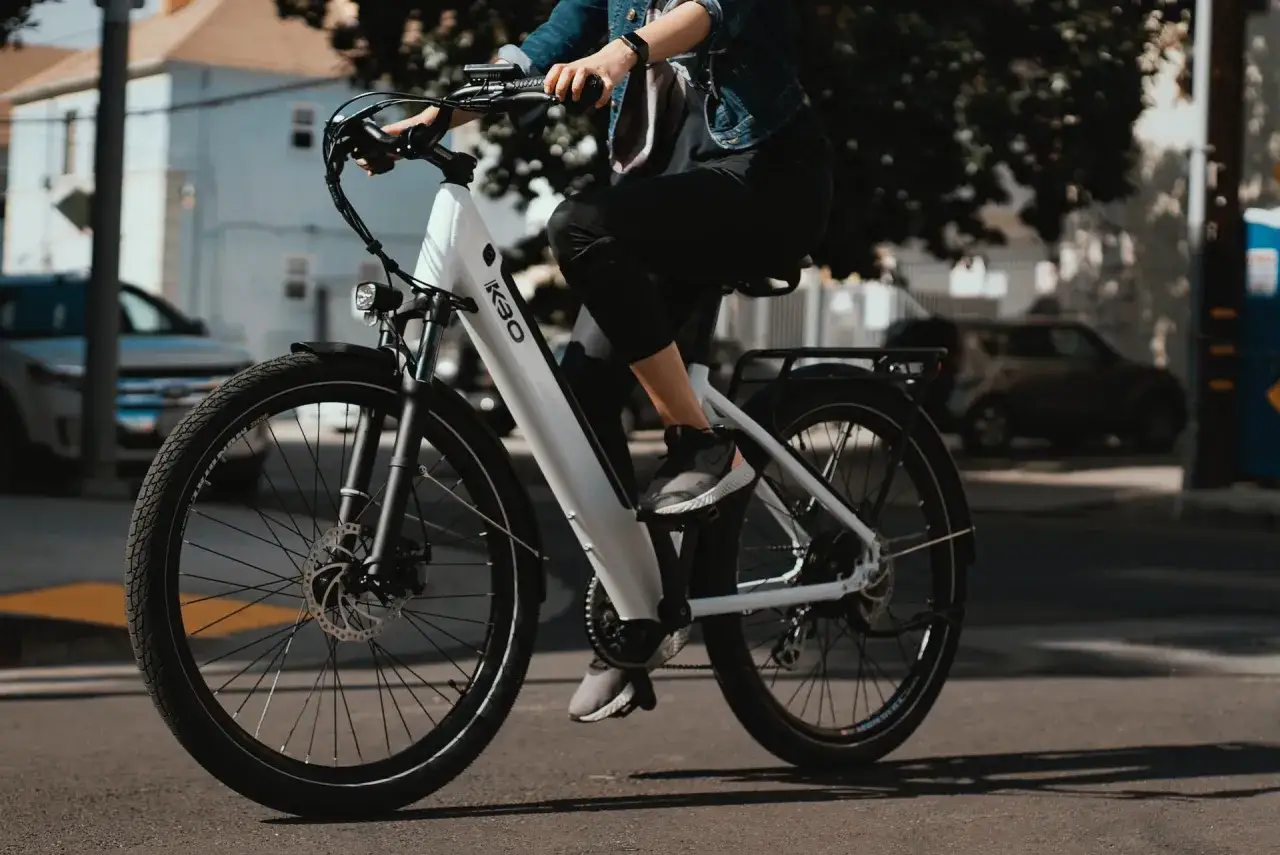 Osoba na białym rowerze elektrycznym K30. Zastanawiasz się, ile kosztuje rower elektryczny? Ten model wygląda na wygodny do jazdy po mieście.