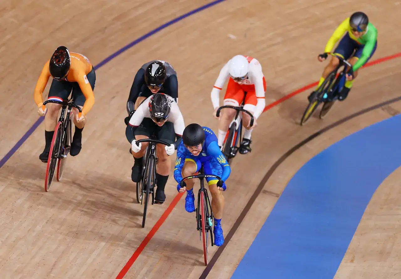 Zawodniczki w kolarstwie torowym podczas wyścigu keirin. Widoczne stroje w barwach narodowych, skupienie na twarzach i dynamiczna jazda.