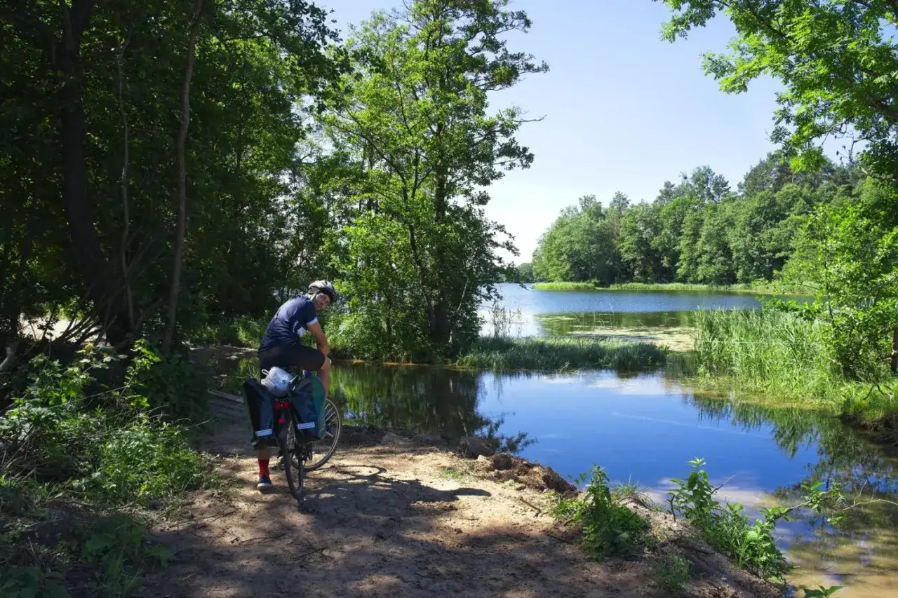 Rowerzysta na tle malowniczego jeziora, odkrywa urokliwe trasy rowerowe Mazury.