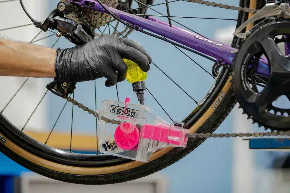 Ręka w czarnej rękawiczce aplikuje smar do łańcucha rowerowego za pomocą specjalnego czyścika. Pytanie: czym smarować łańcuch w rowerze?