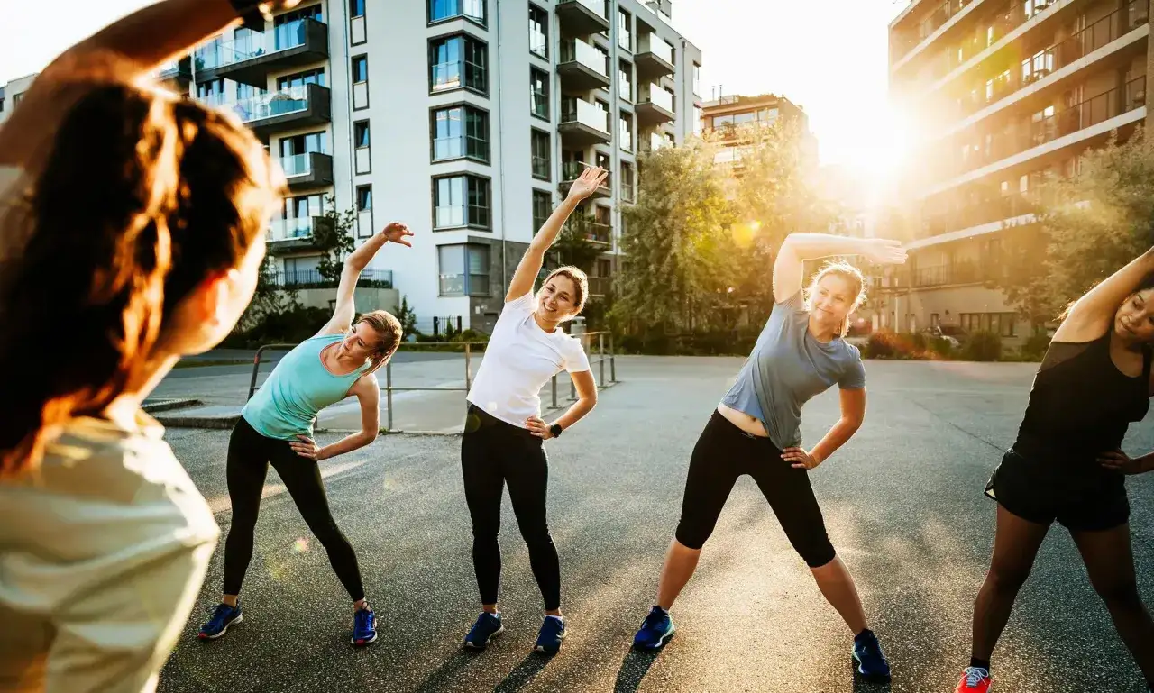 Kobiety wykonują ćwiczenia rozciągające (stretching) na tle nowoczesnych budynków.