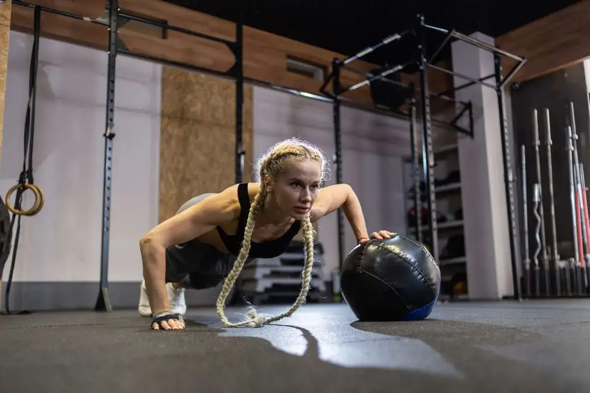 Kobieta wykonuje pompki z piłką lekarską, pokazując, jak ćwiczyć crossfit w domu.