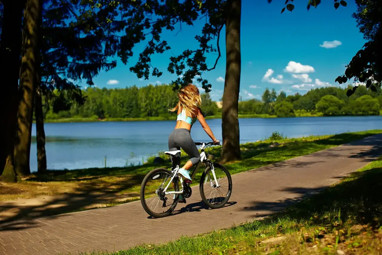 Kobieta na rowerze przemierza malowniczą trasę rowerową wokół jeziora, ciesząc się słonecznym dniem i pięknymi widokami.
