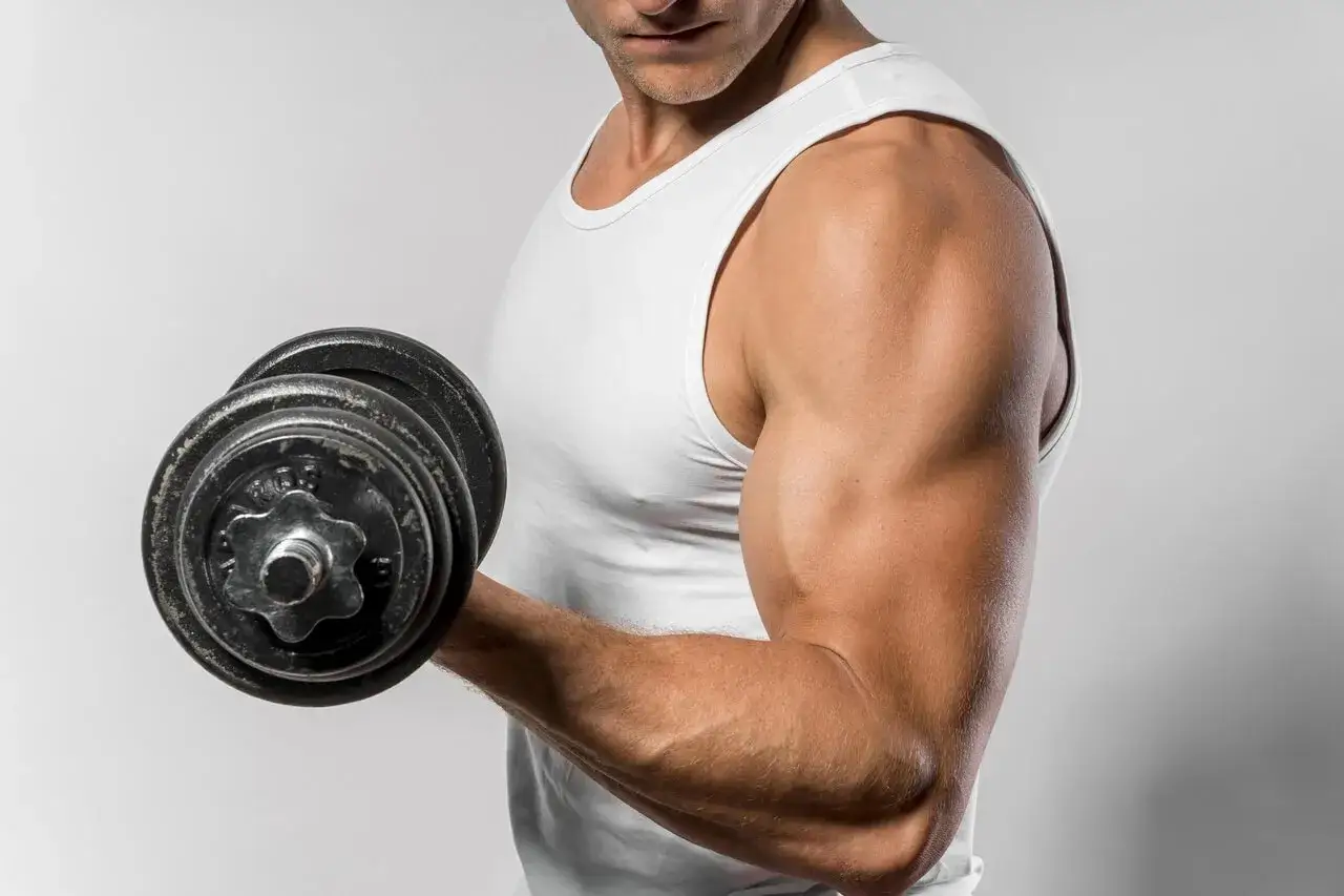 Mężczyzna w białej koszulce podnosi ciężarek, ćwicząc biceps. Ile razy w tygodniu ćwiczyć biceps, by osiągnąć takie efekty?