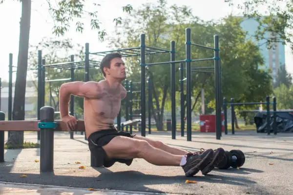 Mężczyzna wykonuje pompki na triceps na ławce na siłowni plenerowej.