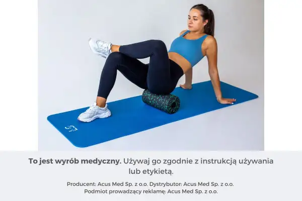 Kobieta na macie rehabilitacyjnej roluje mięsień piramidowy za pomocą wałka.