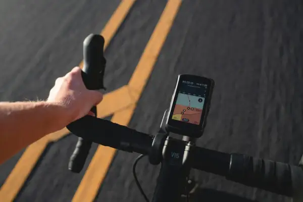 Dłoń trzymająca kierownicę roweru z zamontowanym licznikiem GPS pokazującym mapę.