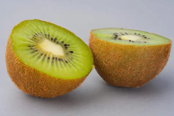 Dwa połówki kiwi na szarym tle. Zastanawiasz się, ile kalorii ma kiwi? To niskokaloryczny owoc, idealny na zdrową przekąskę.