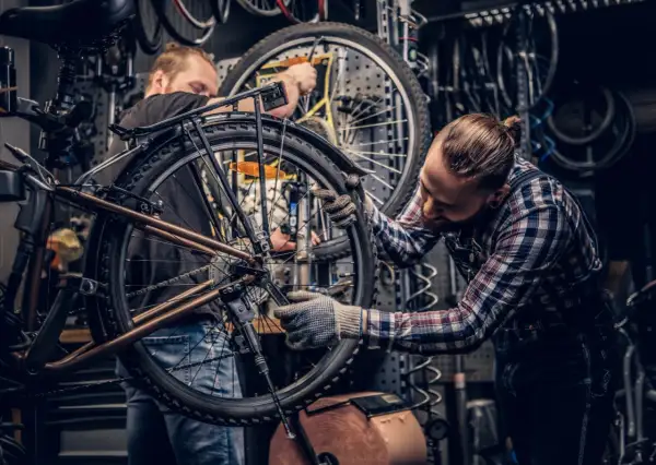 Dwóch mechaników pracuje nad rowerem w warsztacie. Jeden z nich dokonuje konserwacji roweru, dokręcając śruby kluczem.