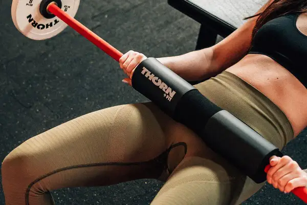 Kobieta wykonuje ćwiczenie hip thrust z gryfem i podkładką.