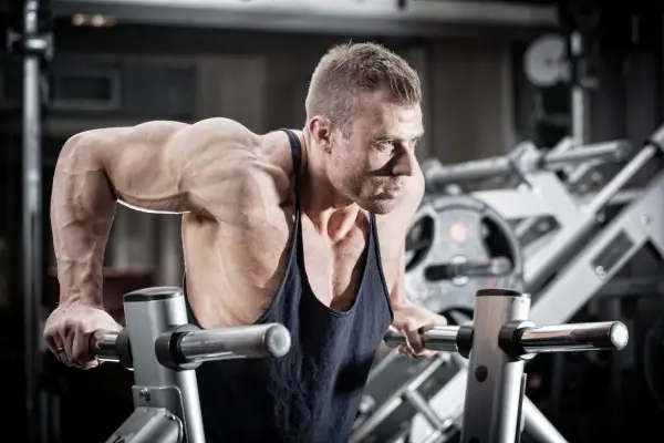 Mięśniowy mężczyzna wykonuje pompki na poręczach, jedno z najlepszych ćwiczeń na triceps.