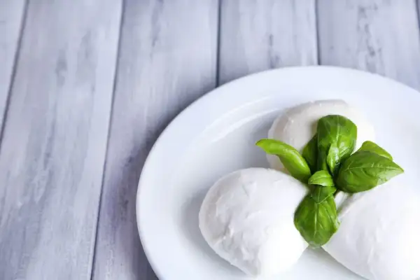 Trzy kulki mozzarelli z listkami bazylii na białym talerzu. Idealne do sałatki, a ich mozzarella kcal są niskie.