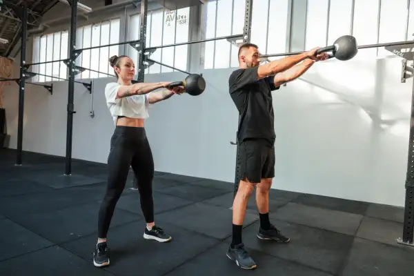 Kobieta i mężczyzna ćwiczą z kettlebellami w siłowni.